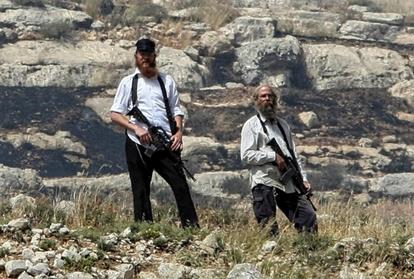 Des colons armés de la colonie de Yitzhar se tiennent sur une falaise surplombant un village palestinien (AFP)