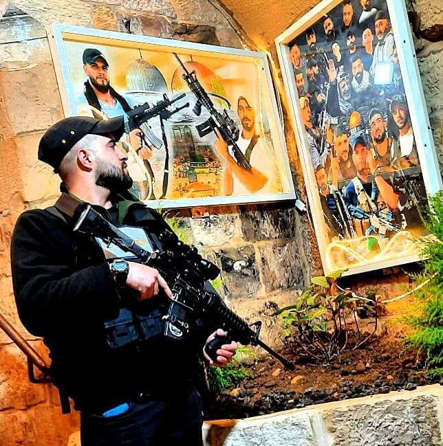 Naplouse. Une photo tirée du profil Facebook de Hussam Isleem, le montrant avec un fusil et debout près des affiches de ses camarades tués du Lion’s Den. (Photo : Médias sociaux)