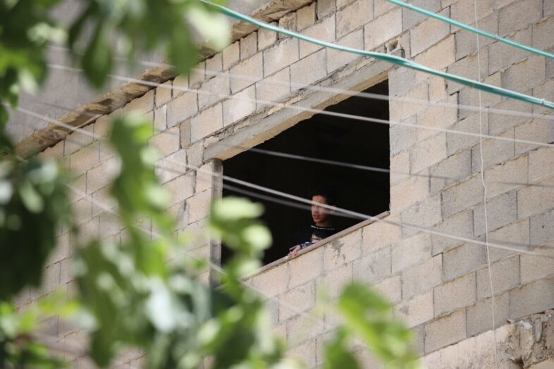 Un jeune homme regarde par la fenêtre d’un bâtiment inachevé. (Photo : Malik Hamamra / Mondoweiss) Camp de réfugiés d’Aida, Cisjordanie occupée, mai 2023. 