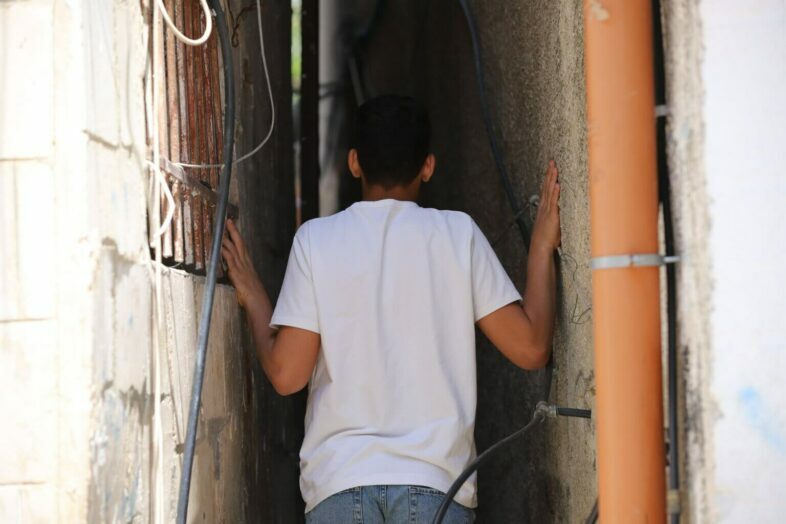 Un adolescent palestinien descend une allée étroite du camp de réfugiés d’Aida. Le camp héberge plus de 6 000 personnes qui vivent dans une zone de 66 hectares (0,66 km²), ce qui en fait un lieu exigu et surpeuplé. Bien des logements du camp sont extrêmement proches les uns des autres, ce qui signifie que les résidents disposent de peu d’intimité à l’intérieur même de leur propre logement. (Photo : Malik Hamamra / Mondoweiss) Camp de réfugiés d’Aida, Cisjordanie occupée, mai 2023. 