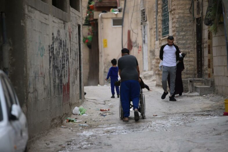 Un garçon promène son ami en chaise roulante dans les rues du camp. (Photo : Malik Hamamra / Mondoweiss) Camp de réfugiés d’Aida, Cisjordanie occupée, mai 2023. 