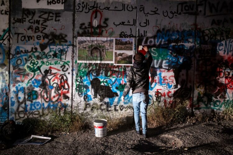 À la lumière des phares de sa voiture, Ahmad al-Bazz déploie son exposition sur le mur d’annexion israélien à Bethléem, près du camp de réfugiés d’Aida. (Photo : Anne Paq)