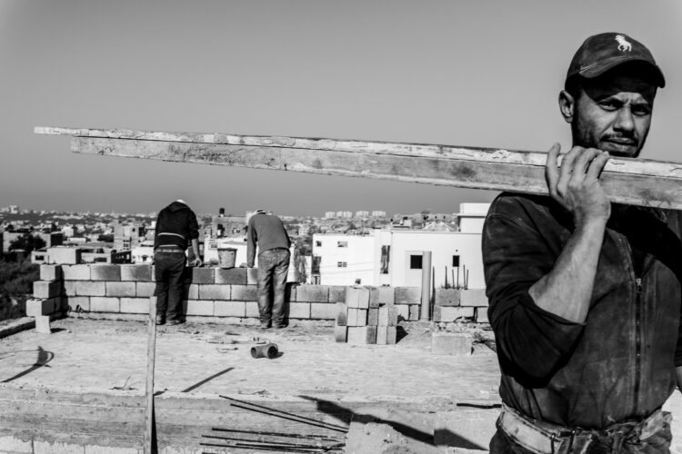 Un ouvrier porte une pièce en bois au moment où, à l’arrière-plan, le « moalem » – ou chef d’équipe – donne ses instructions à un collègue. Beit Hanoun, 11 décembre 2022