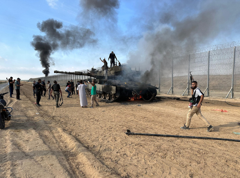 Les combattants du Hamas envahissent Israël : Ce 7 octobre 2023, des Palestiniens grimpent sur un char israélien en flammes à proximité de la clôture de frontière entre Gaza et Israël.