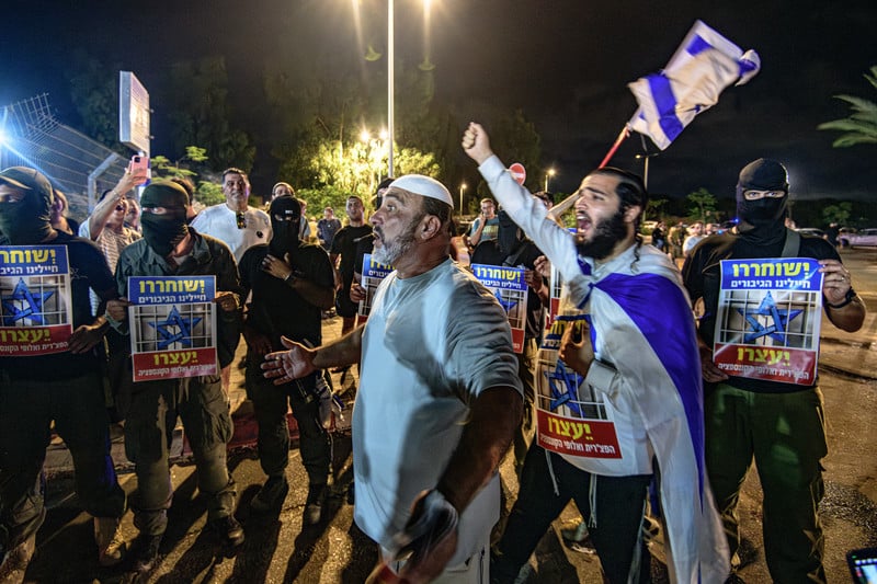 Viol, torture et meurtre : le quotidien des camps de concentration israéliens. Photo : 30 juillet 2024, base militaire de Beit Lid. Des Israéliens, dont des réservistes masqués, se sont rassemblés afin de soutenir les soldats accusés d'avoir violé un détenu palestinien, et brandissent des pancartes sur lesquelles on peut lire : « Les soldats héroïques devraient être relâchés ».