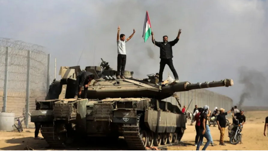 Du Tunnel de la liberté au déluge d’Al-Aqsa : Prisonniers, résistance et libération. Photo : Des Palestiniens de Gaza se tiennent sur un char sioniste capturé, le 7 octobre 2023