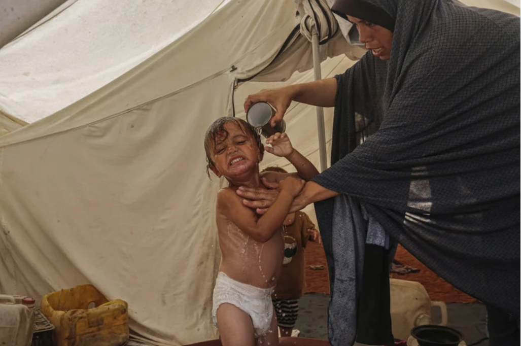 10 juillet 2024. Une femme lave sa petite fille avec une tasse d'eau dans leur abri de fortune à Deir al-Balah on 10 July. Israël a coupé la distribution d'eau et a bombardé ses sites, provoquant ainsi une chute de 94 pour 100 de la fourniture d'eau à Gaza.