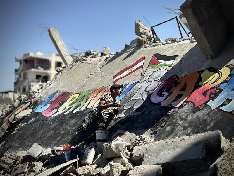 Pourquoi le massacre de civils est-il une stratégie délibérée d'Israël ? Photo :26 septembre 2024. Jamil al-Baz, un Palestinien déplacé, peint une fresque sur les décombres de bâtiments détruits à Khan Younis, dans le sud de la bande de Gaza.