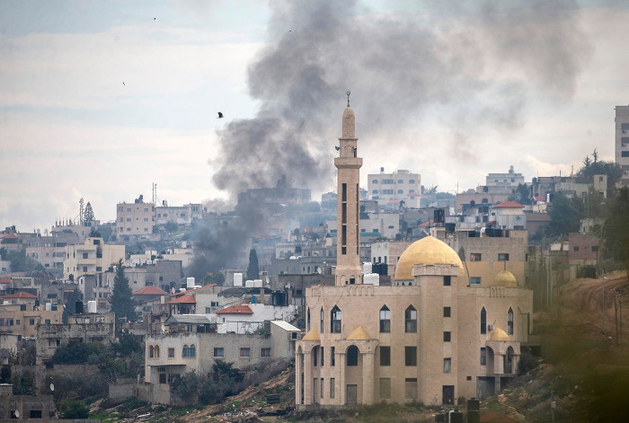 L’État génocidaire tourne maintenant le maximum de sa violence vers la Cisjordanie. Photo : 24 janvier 2025 – Des fumées s’élèvent au-dessus du camp de réfugiés de Jénine alors que les forces coloniales israéliennes poursuivent leur raid sur Jénine et le camp pour la quatrième journée dans le cadre d’une opération militaire majeure visant à réprimer la résistance armée. Des bulldozers armés israéliens ont pénétré dans le camp, détruisant les infrastructures et les habitations. Des témoins rapportent que certaines maisons sont brûlées par les forces israéliennes. Des drones survolent constamment le camp, surveillant et filmant les nombreuses familles palestiniennes qui ont été forcées de fuir ces derniers jours. Les entrées et les sorties sont bloquées par les forces israéliennes, empêchant les travailleurs de la santé et les journalistes de pénétrer dans le camp de réfugiés. Au moins 12 Palestiniens ont été assassinés et près de 40 blessés lors de l’assaut israélien sur Jénine – Photo : Wahaj Bani Moufleh / Activestills