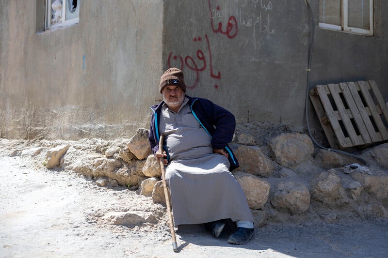 Le 30 mars 2025, quelques jours après une attaque des colons, un habitant palestinien de Jinba, un village de la zone de Masafer Yatta, dans le sud de la Cisjordanie occupée, est assis contre un mur couvert de graffitis disant : « Nous resterons ici ! »