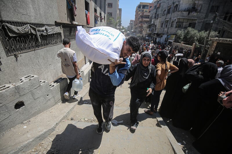 Pas de trêve en vue alors que les enfants de Gaza succombent à la famine. Photo : Un homme porte un sac de farine pendant que d'autres font la file à un point de distribution d'aide à Gaza même, le 26 juin.