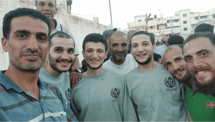 Deux frères nous parlent de leur détention. Photo : 13 octobre 2025. Première rangée, troisième et quatrième à partir de la droite : Hady et Mumin Thaher – derrière eux, leur père Adham – en compagnie de leur cousin Muhammad Thaher. Hady, Mumin et Muhammad portent encore l'uniforme gris de la prison. Ils viennent d'être libérés de leur détention en Israël.